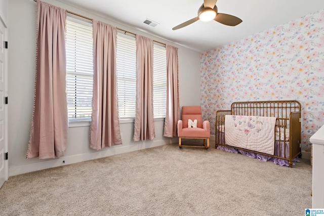 carpeted bedroom with a crib and ceiling fan