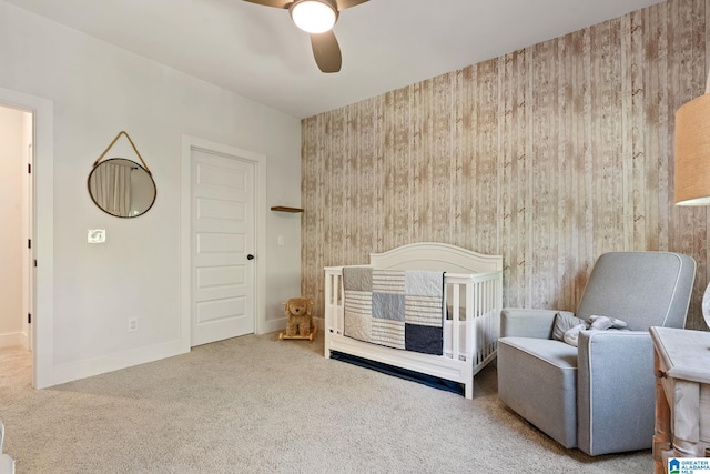 carpeted bedroom with a crib, ceiling fan, and wood walls