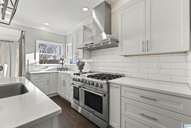 kitchen featuring white cabinets, ornamental molding, range with two ovens, and wall chimney exhaust hood