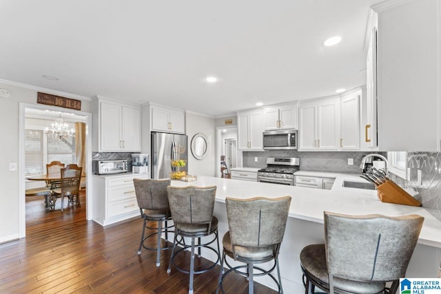 kitchen with sink, kitchen peninsula, a breakfast bar area, white cabinets, and appliances with stainless steel finishes