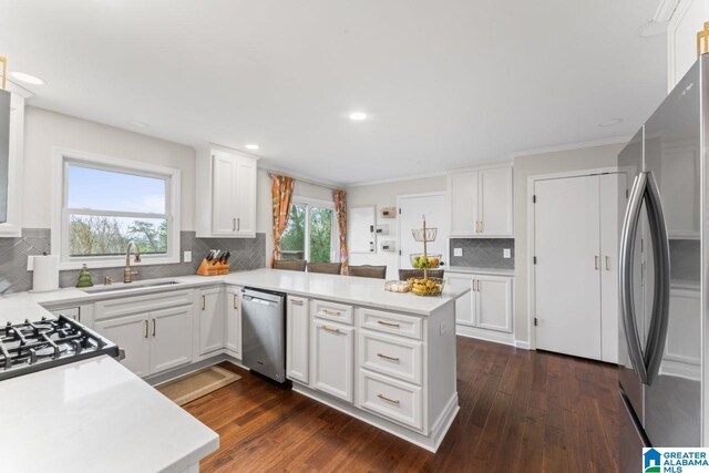 kitchen featuring sink, tasteful backsplash, kitchen peninsula, white cabinets, and appliances with stainless steel finishes