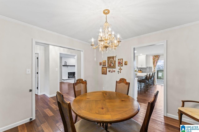 dining room featuring a brick fireplace, dark hardwood / wood-style floors, ornamental molding, and an inviting chandelier