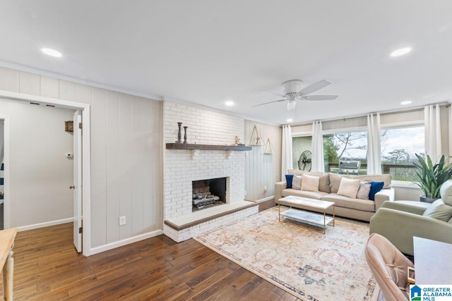 living room with crown molding, ceiling fan, a fireplace, and dark wood-type flooring