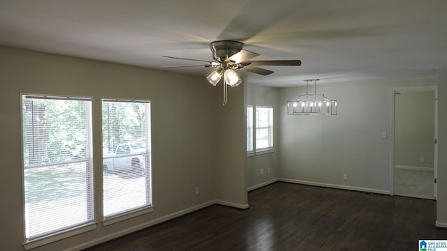 empty room featuring a wealth of natural light, dark hardwood / wood-style flooring, and ceiling fan with notable chandelier