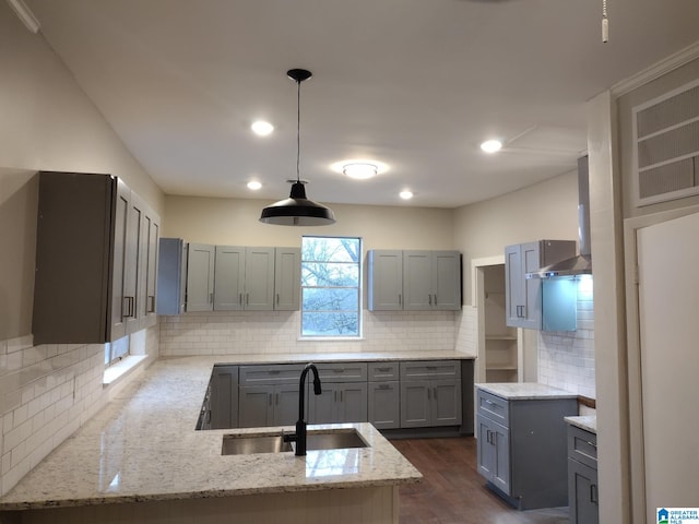 kitchen with pendant lighting, gray cabinetry, sink, wall chimney exhaust hood, and tasteful backsplash