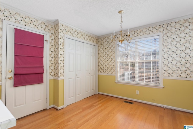 unfurnished bedroom featuring a closet, wood-type flooring, a chandelier, and ornamental molding