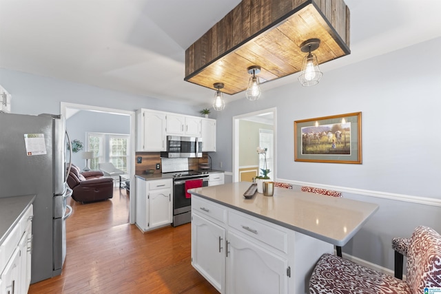 kitchen featuring white cabinets, light hardwood / wood-style floors, hanging light fixtures, and appliances with stainless steel finishes