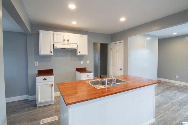 kitchen with a kitchen island with sink, sink, white cabinets, dark hardwood / wood-style floors, and butcher block counters