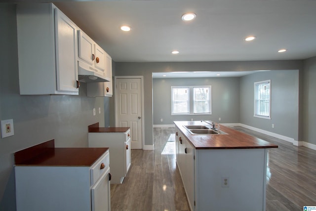 kitchen featuring wooden counters, sink, wood-type flooring, a center island with sink, and white cabinetry