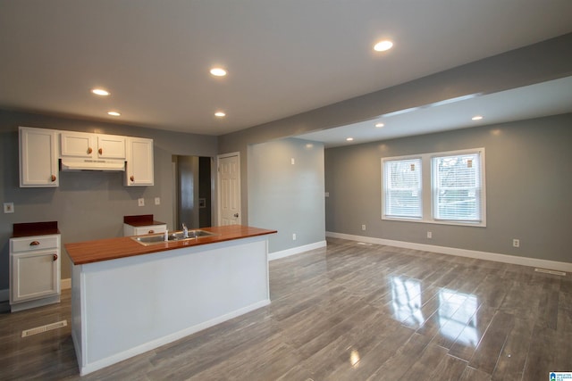 kitchen with dark wood-type flooring, sink, white cabinets, butcher block countertops, and a kitchen island