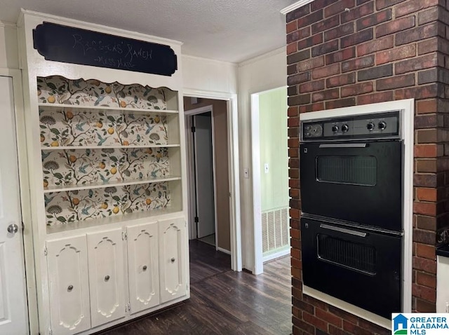 kitchen with white cabinetry, dark wood-type flooring, double oven, a textured ceiling, and ornamental molding