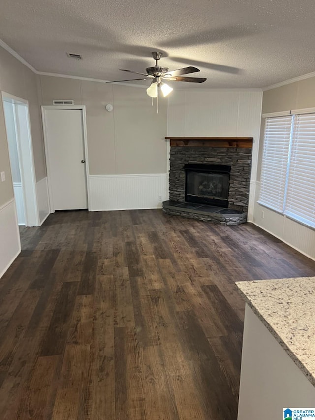 unfurnished living room with a stone fireplace, crown molding, ceiling fan, and a textured ceiling