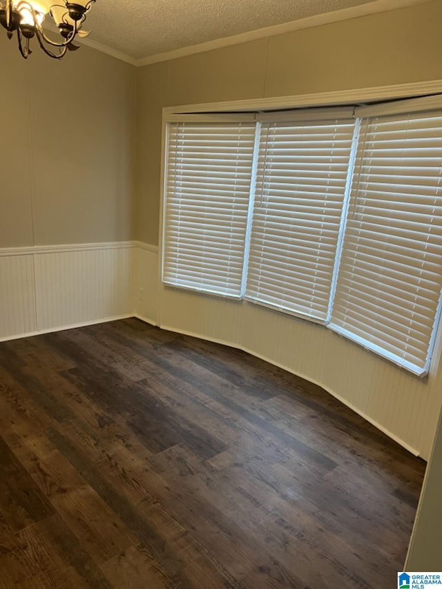 unfurnished room featuring a textured ceiling, dark wood-type flooring, crown molding, and a notable chandelier