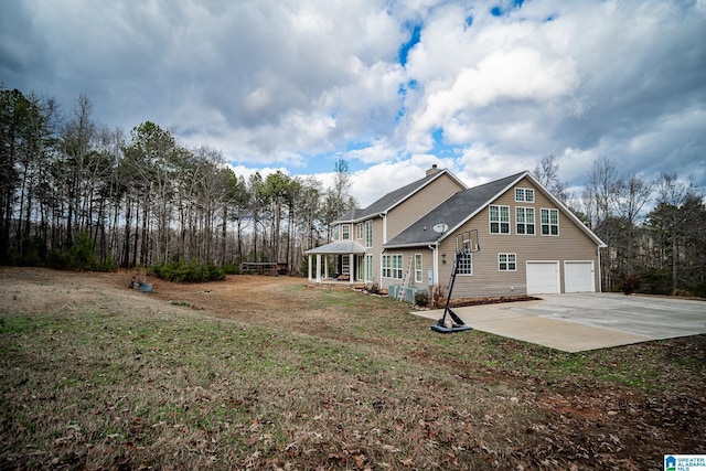 exterior space featuring a chimney, an attached garage, concrete driveway, and a yard