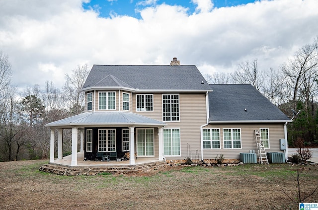 rear view of house with a shingled roof, a patio, central air condition unit, and a chimney