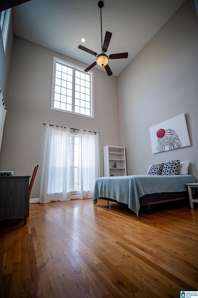 unfurnished bedroom featuring baseboards, recessed lighting, a towering ceiling, wood finished floors, and a ceiling fan