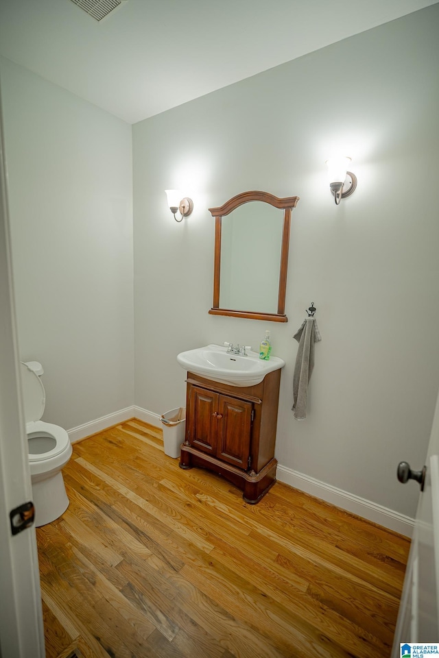 bathroom featuring vanity, wood finished floors, visible vents, baseboards, and toilet