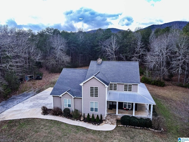 traditional-style house with a view of trees, a mountain view, driveway, and a chimney