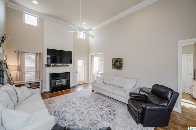 living room featuring wood-type flooring, a towering ceiling, ceiling fan, and crown molding