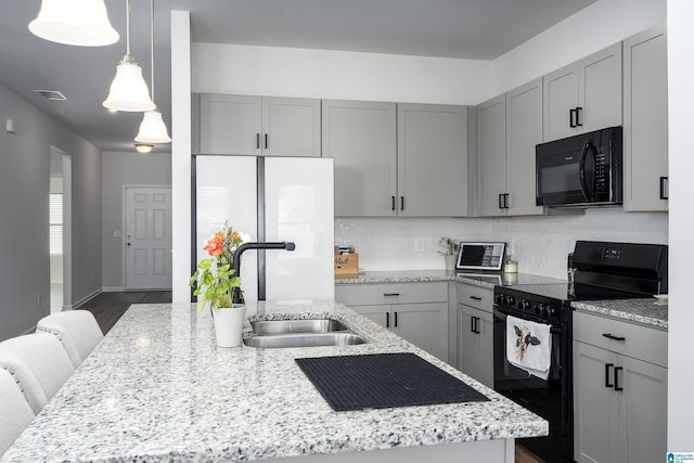 kitchen featuring backsplash, gray cabinetry, a center island with sink, and black appliances