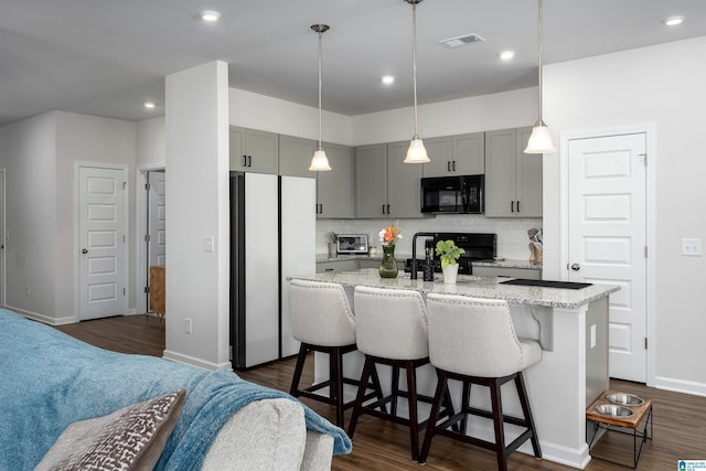 kitchen with backsplash, light stone counters, black appliances, a center island with sink, and gray cabinets