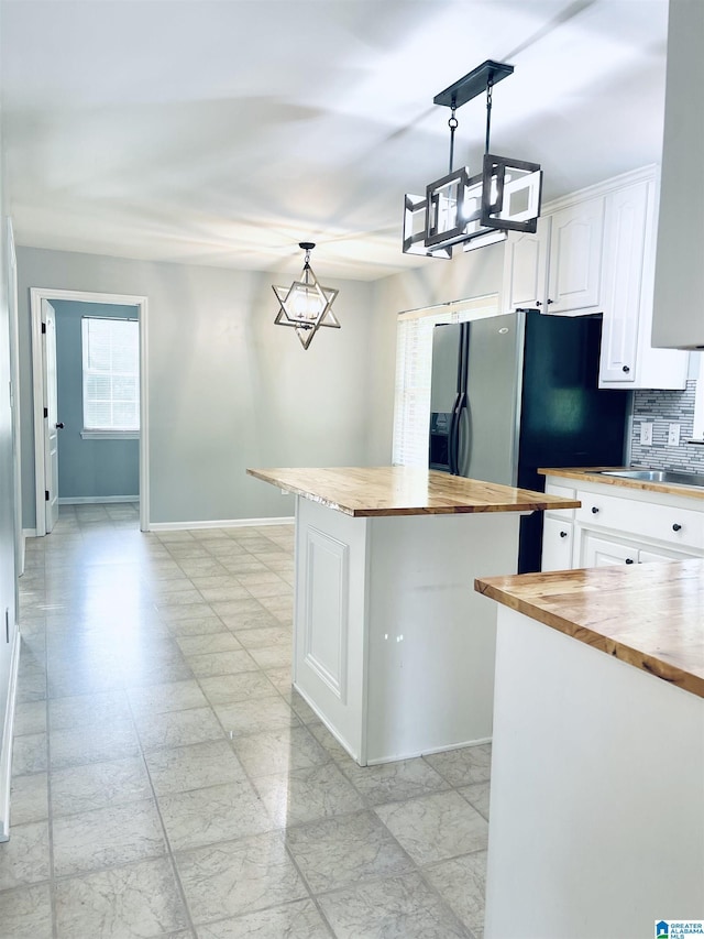 kitchen featuring a center island, butcher block counters, decorative backsplash, decorative light fixtures, and white cabinetry