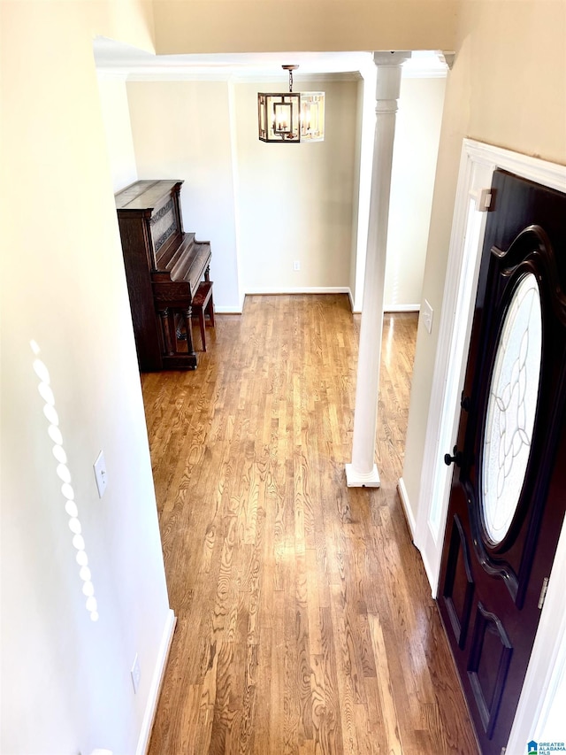 foyer entrance featuring decorative columns, a notable chandelier, and light wood-type flooring