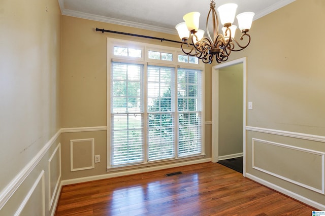 spare room featuring dark hardwood / wood-style flooring, an inviting chandelier, a healthy amount of sunlight, and crown molding