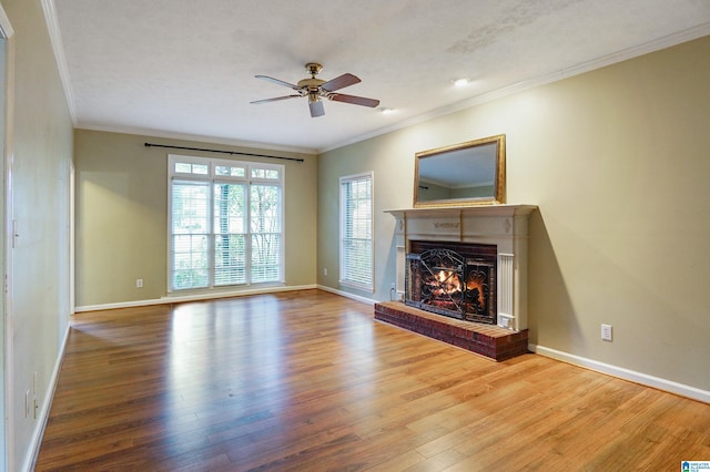 unfurnished living room featuring wood-type flooring, a brick fireplace, ceiling fan, and crown molding