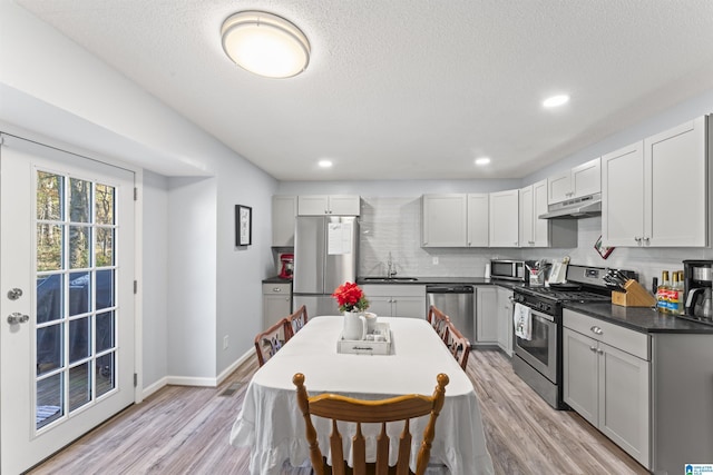 kitchen featuring a textured ceiling, stainless steel appliances, light hardwood / wood-style floors, sink, and backsplash