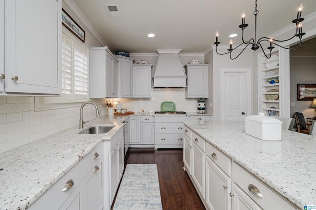 kitchen with sink, an inviting chandelier, light stone counters, white cabinets, and custom exhaust hood