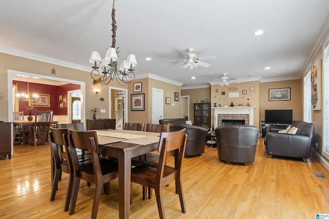 dining room with ceiling fan with notable chandelier, light hardwood / wood-style floors, crown molding, and a brick fireplace