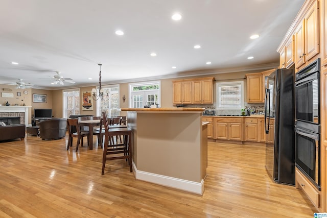 kitchen featuring a kitchen breakfast bar, black appliances, light brown cabinets, a fireplace, and light hardwood / wood-style floors