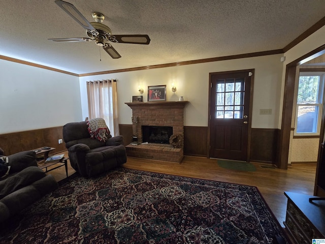 living room featuring ceiling fan, a fireplace, crown molding, and a textured ceiling