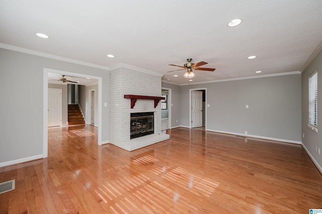 unfurnished living room with a brick fireplace, ceiling fan, wood-type flooring, and ornamental molding