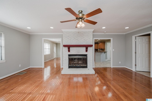 unfurnished living room with ceiling fan, a brick fireplace, ornamental molding, a textured ceiling, and light wood-type flooring