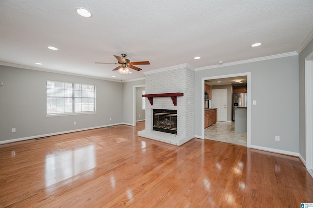 unfurnished living room featuring ceiling fan, light hardwood / wood-style flooring, crown molding, a textured ceiling, and a fireplace