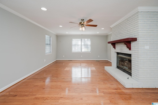 unfurnished living room featuring a brick fireplace, a textured ceiling, ceiling fan, crown molding, and light hardwood / wood-style floors