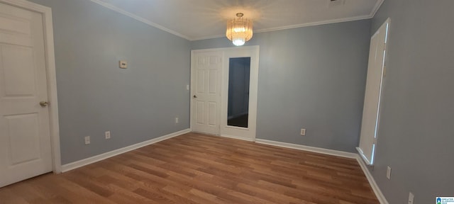 empty room featuring hardwood / wood-style flooring, ornamental molding, and an inviting chandelier