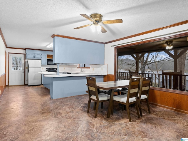 dining area featuring ceiling fan, wooden walls, a textured ceiling, and ornamental molding