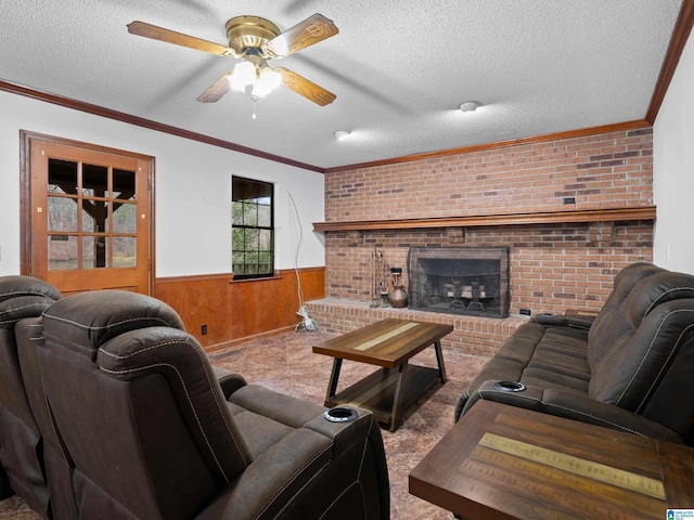 living room featuring wood walls, crown molding, ceiling fan, a textured ceiling, and a fireplace