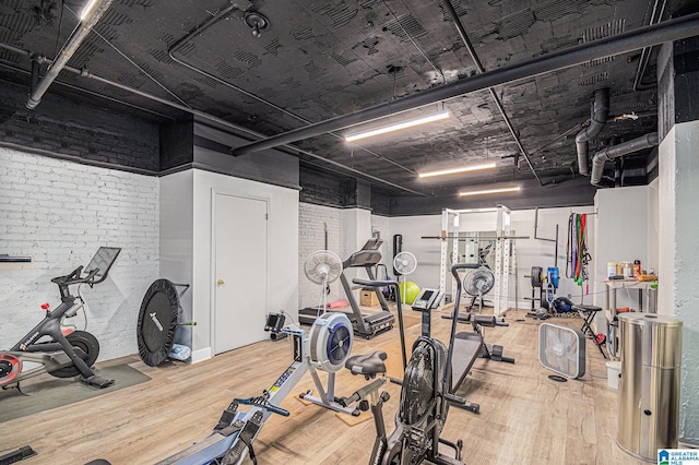 gym with hardwood / wood-style flooring and brick wall