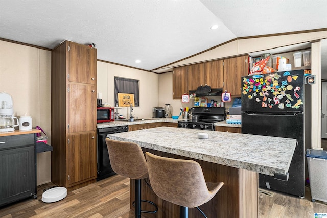 kitchen featuring lofted ceiling, black appliances, a kitchen breakfast bar, hardwood / wood-style flooring, and a textured ceiling