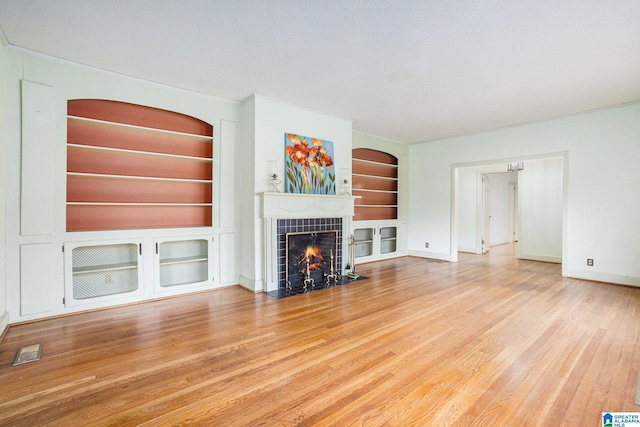 unfurnished living room featuring a tile fireplace, built in features, and light hardwood / wood-style flooring