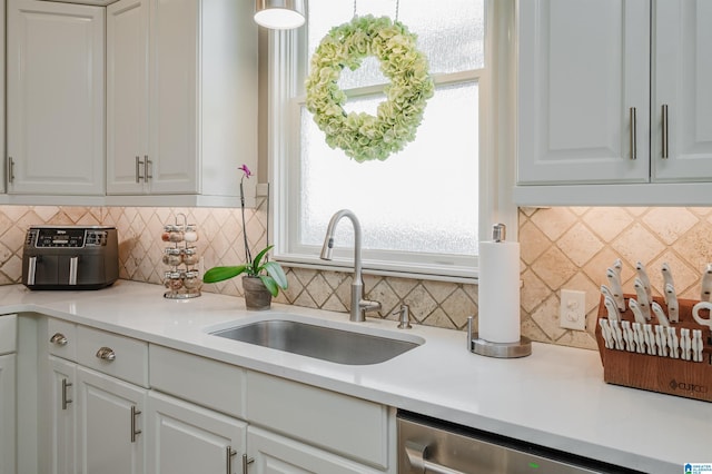 kitchen featuring decorative backsplash, white cabinetry, dishwasher, and sink