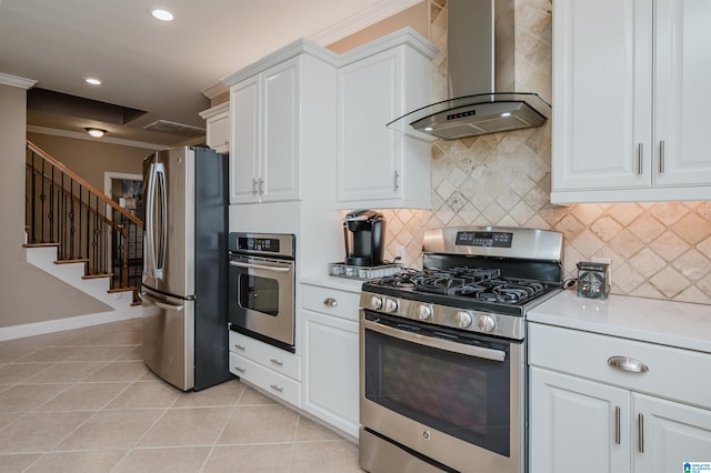 kitchen with white cabinets, wall chimney exhaust hood, light tile patterned floors, ornamental molding, and appliances with stainless steel finishes