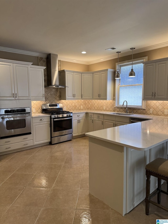 kitchen with a kitchen breakfast bar, sink, wall chimney exhaust hood, appliances with stainless steel finishes, and decorative light fixtures