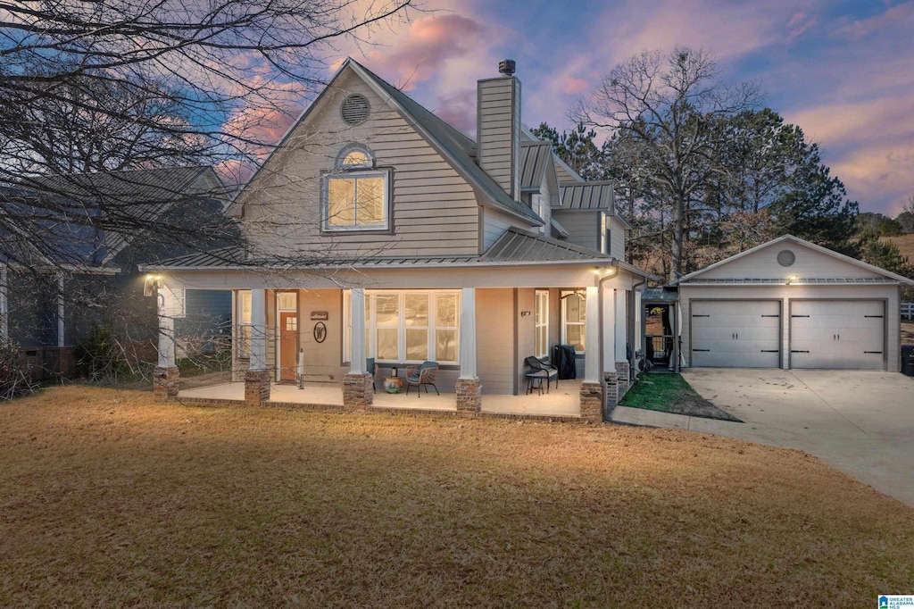 back house at dusk featuring a lawn, a patio, an outdoor structure, and a garage