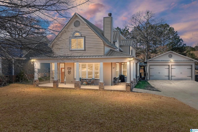 back house at dusk featuring a lawn, a patio, an outdoor structure, and a garage