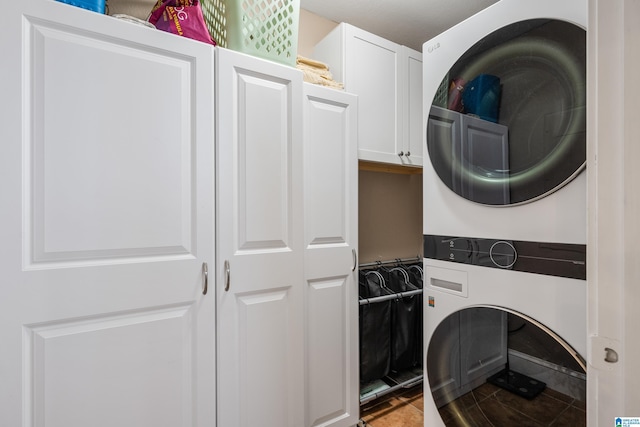 laundry area with tile patterned flooring, cabinets, and stacked washing maching and dryer